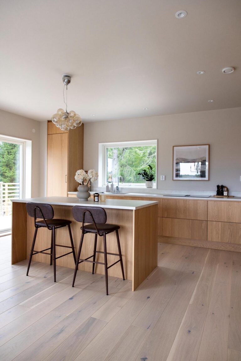 Ljust kök med köksö och öppen planlösning i ett nybyggt hus.