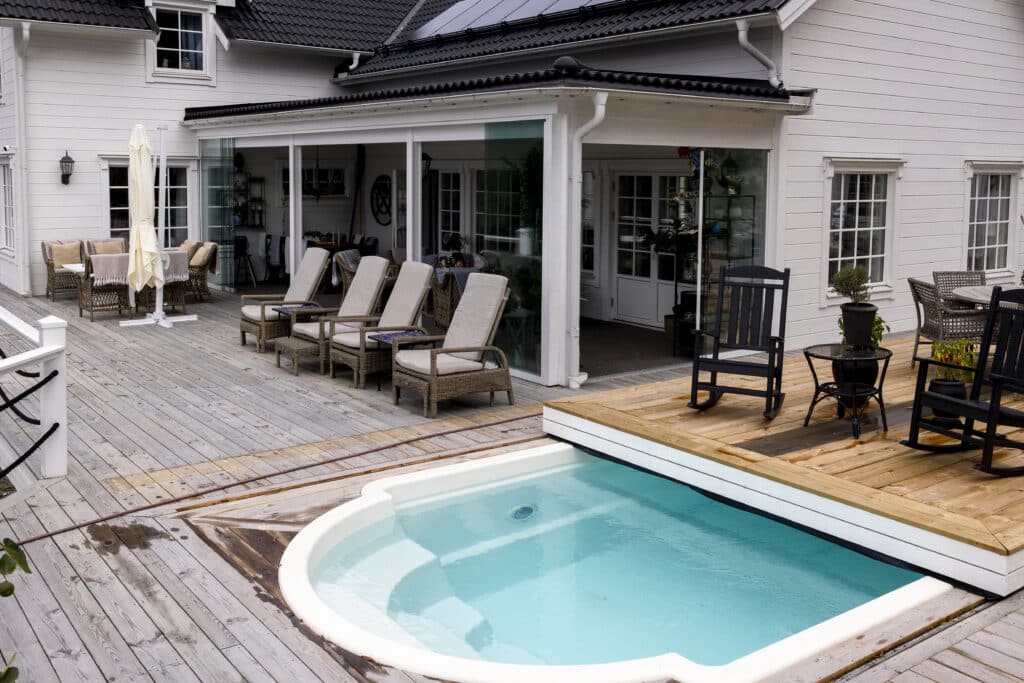 Stort inglasat uterum och altan i trä med inbyggd pool vid ett vitt trähus, vilket visar hur smart husplacering ger plats för framtida trädgårdsprojekt och uteplatser.
